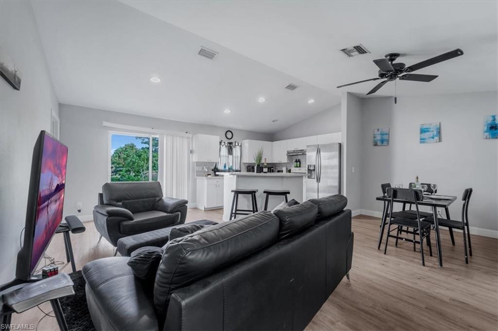 Open-concept living space featuring vaulted ceilings, recessed lighting, wood-finish flooring, a contemporary ceiling fan, and sliding glass doors to the exterior