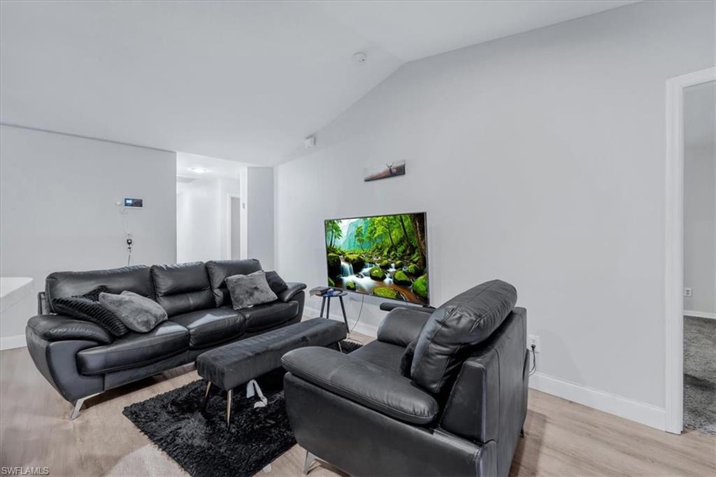 Living area featuring wood-finish flooring, vaulted ceiling, recessed lighting, and white baseboards
