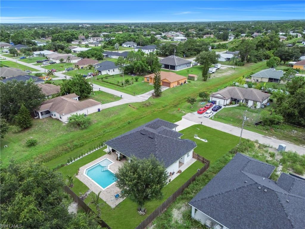 Fenced backyard featuring a rectangular swimming pool with stone paver surround, mature landscaping, and an expansive lawn