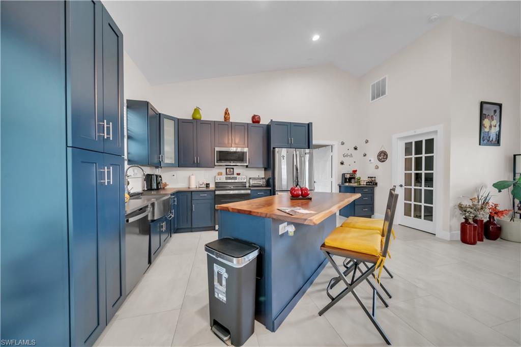 Kitchen featuring blue shaker-style cabinetry, stainless steel appliances, a wood butcher block island, and light-toned tile flooring