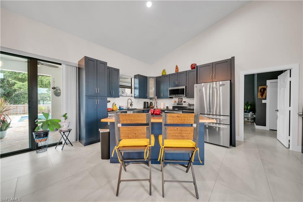 Kitchen featuring dark blue cabinetry, stainless steel appliances, a center island with a wood-finish countertop, and light-toned tile flooring