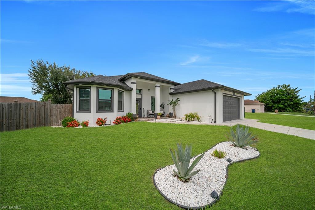 Contemporary stucco exterior featuring a dark gray garage door, a prominent front entrance with large columns, a bay window with dark trim, and a well-maintained green lawn