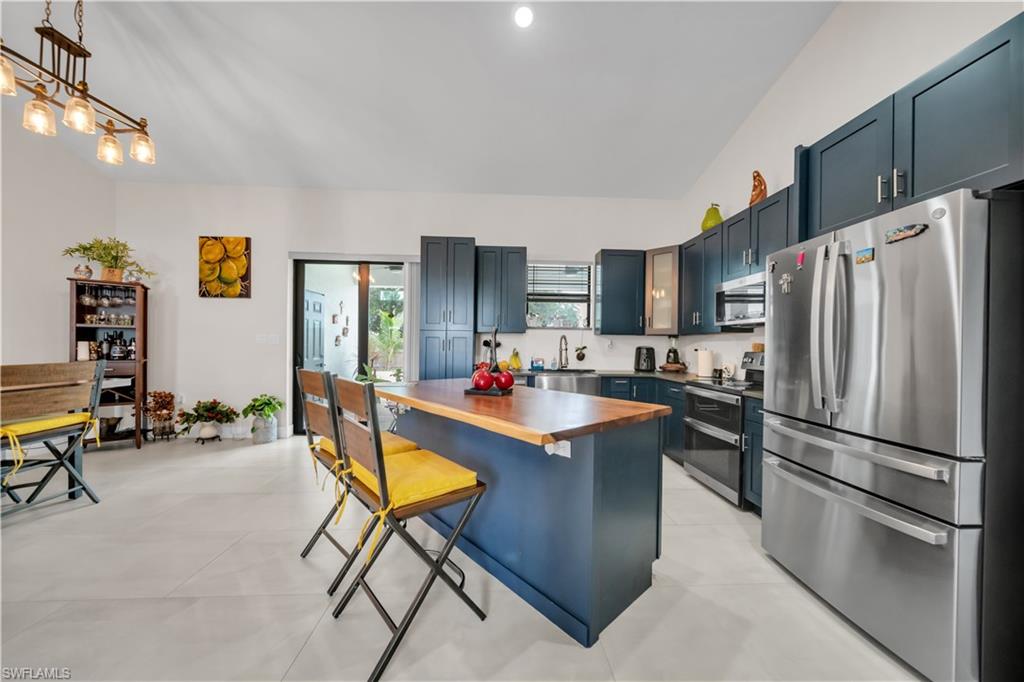 Kitchen featuring a central island with a wood-finish countertop, dark blue cabinetry, stainless steel appliances, and a vaulted ceiling