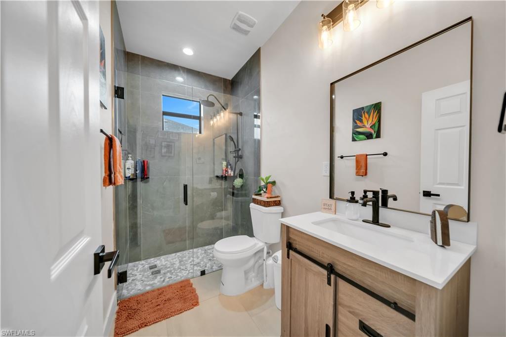 Bathroom featuring a frameless glass shower enclosure with gray tile surround, pebble flooring, and a window
