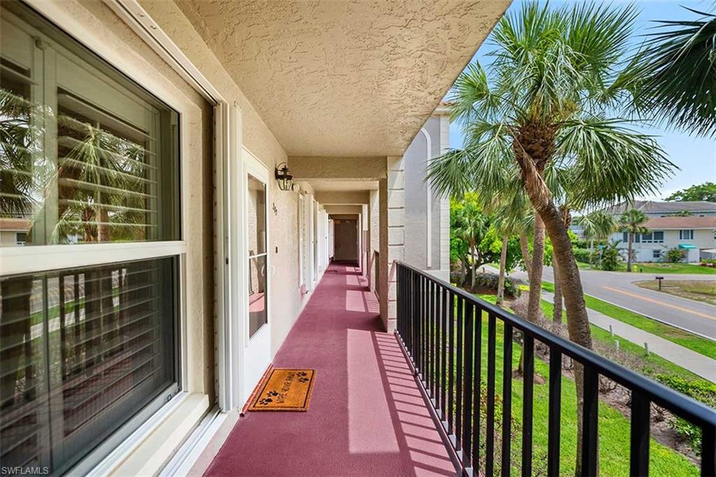 Exterior balcony with a black metal railing overlooking a street and mature palm trees
