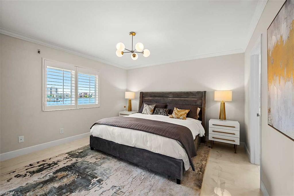 Bedroom featuring light-toned walls, crown molding, and a visible body of water through horizontal slat window treatments