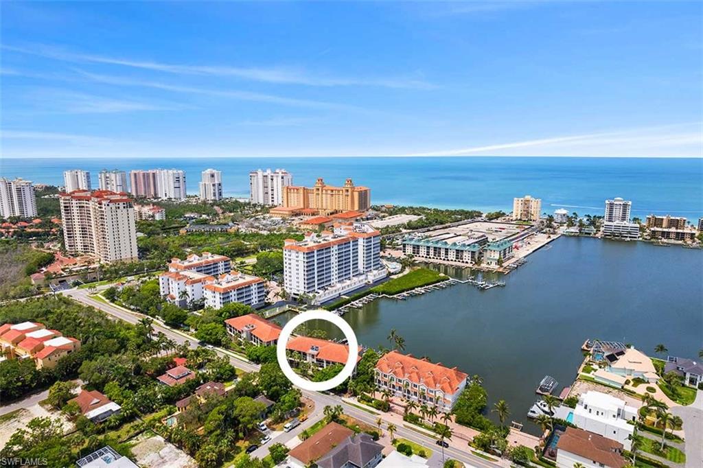 Aerial perspective showcasing a coastal community with multiple high-rise and mid-rise buildings, a large body of water with boats, and distant ocean presence