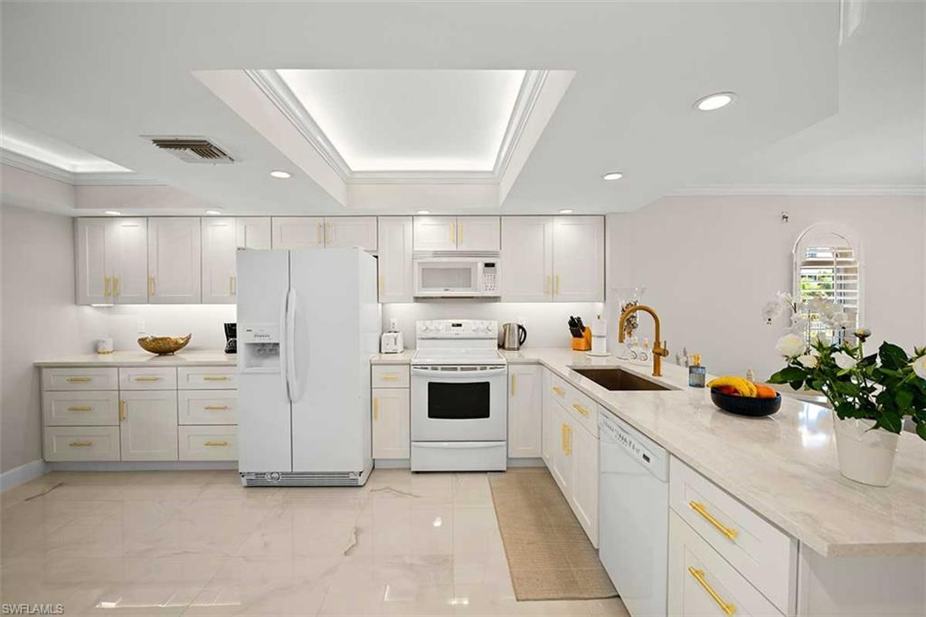 Contemporary kitchen featuring an integrated skylight, recessed lighting, white cabinetry with gold-finish hardware, light-toned stone countertops, and a gold-finish gooseneck faucet