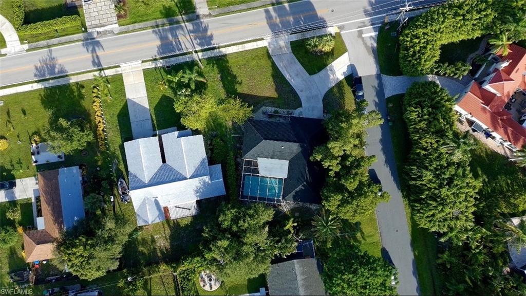 Aerial property view featuring a light grey shingle roof, concrete driveway, and a fenced swimming pool