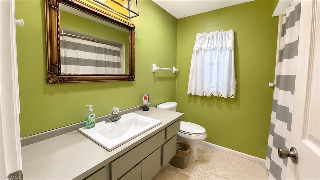Bathroom featuring a vanity with an integrated sink, a large ornate framed mirror, a toilet, and light-toned floor tiles