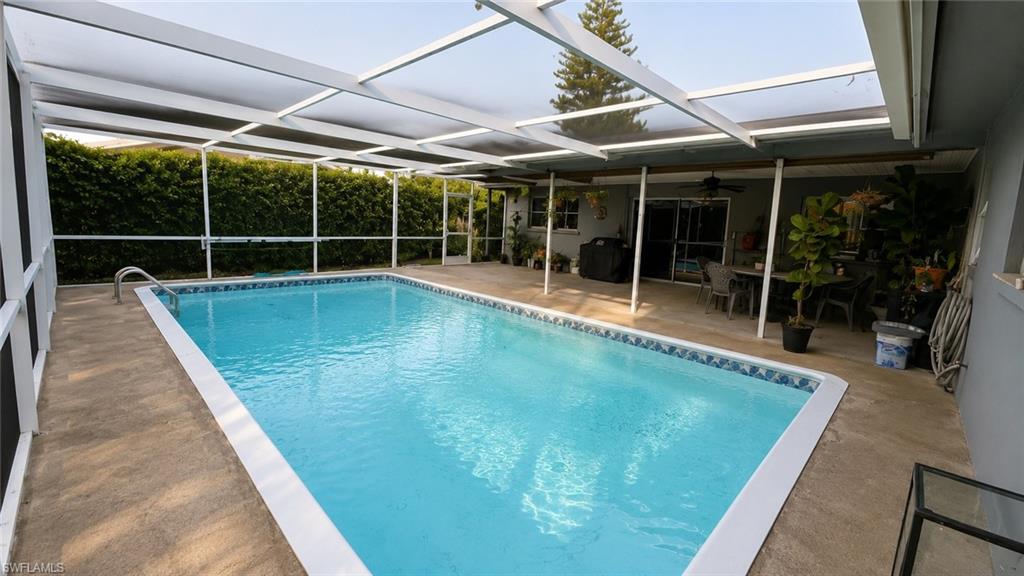 Screened swimming pool enclosure featuring a rectangular pool with a concrete deck, an integrated covered patio, and mature perimeter hedging