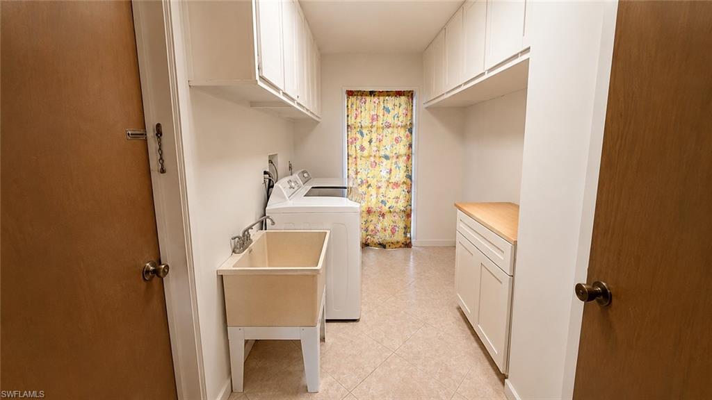 Utility room featuring a built-in wash basin, white upper cabinetry, white lower cabinetry with a wood-finish countertop, and tile flooring