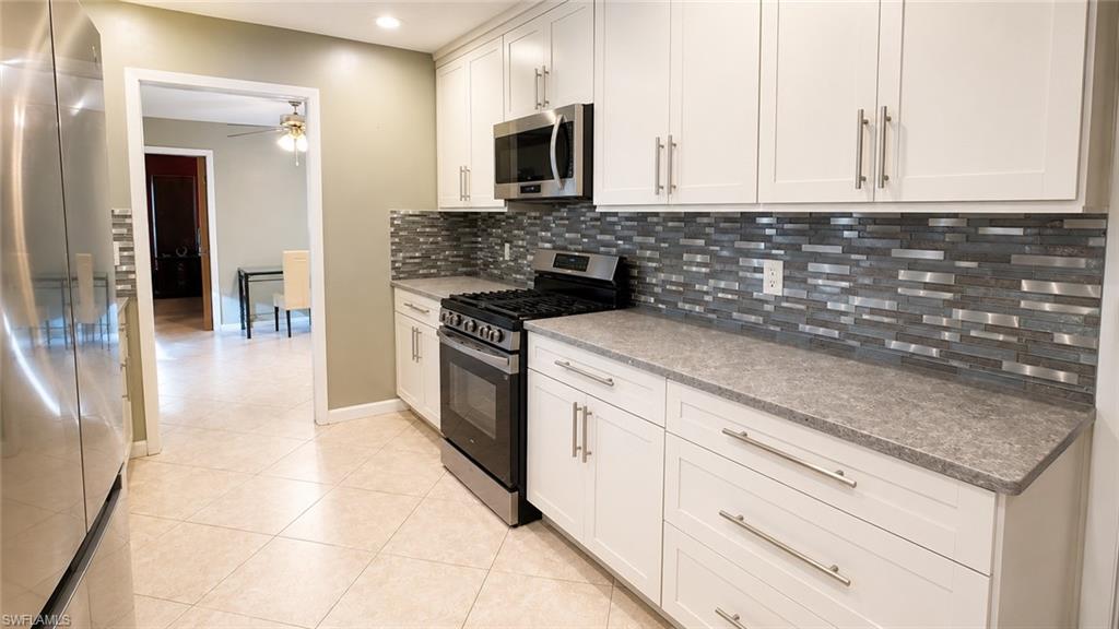 Kitchen featuring white cabinetry with brushed nickel hardware, a stainless steel gas range, a mosaic tile backsplash, and light-toned tile flooring