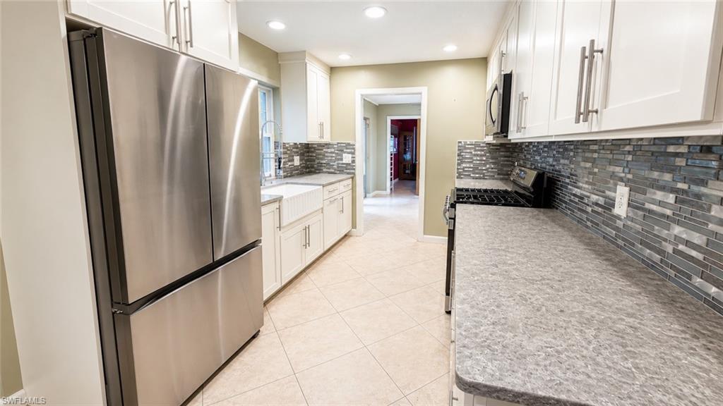 Kitchen featuring stainless steel appliances, white cabinetry, a farmhouse sink, tile flooring, and a mosaic tile backsplash