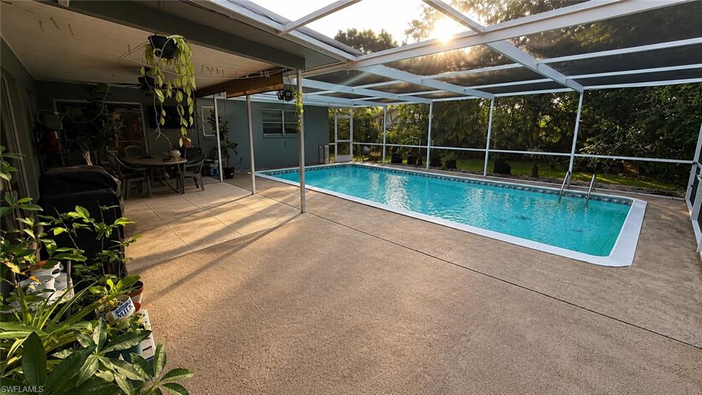 Screened pool enclosure featuring an in-ground swimming pool, an expansive concrete deck, and a covered patio area with tiled flooring