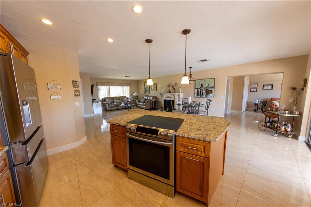 Kitchen with wood finish cabinetry, open floor plan, stainless steel appliances, and light stone counters