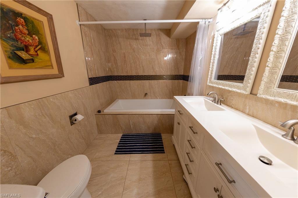 Bathroom featuring tile walls, a combined bath / shower with rainfall shower, double vanity, and light tile patterned floors