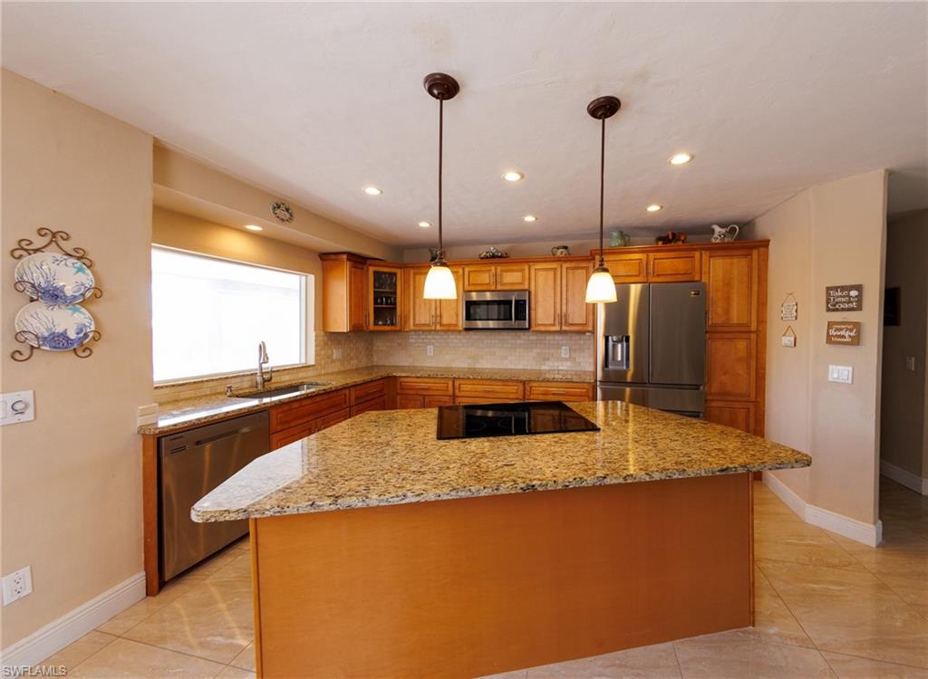Kitchen with stainless steel appliances, a center island, decorative light fixtures, light stone counters, and decorative backsplash