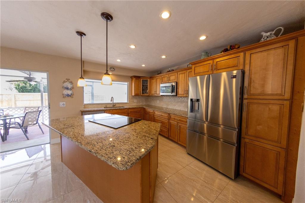 Kitchen featuring stainless steel appliances, wood finish cabinetry, dark stone counters, hanging light fixtures, and tasteful backsplash