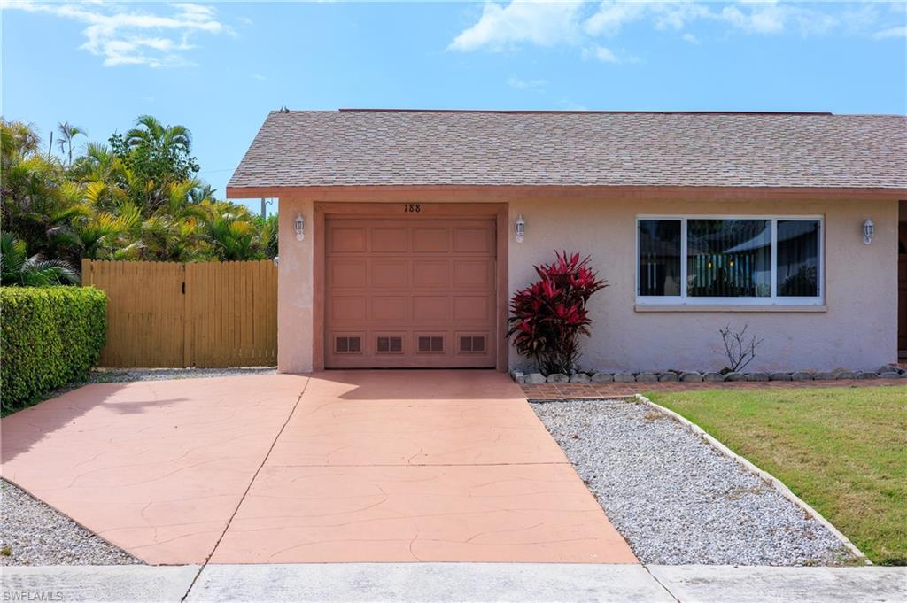 View of front facade with stucco siding, an attached garage, driveway, roof with shingles, and a gate