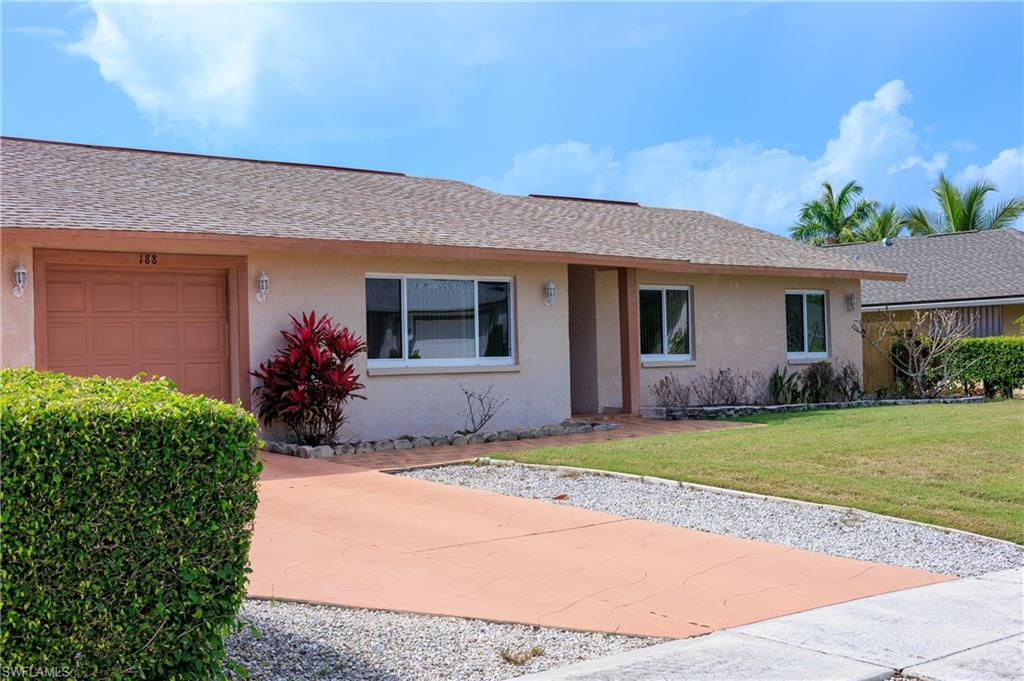 Ranch-style house featuring stucco siding, a front lawn, an attached garage, roof with shingles, and driveway