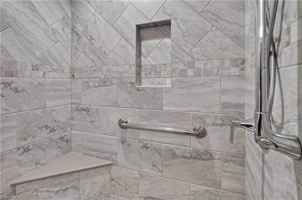 Shower with large format stone-look tile, accent band, built-in niche, and corner bench