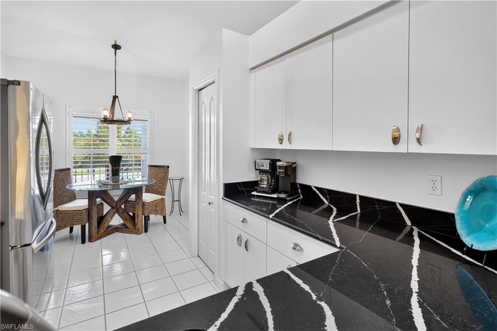 White cabinetry, black countertops with white veining, white tile flooring, and a window with plantation shutters