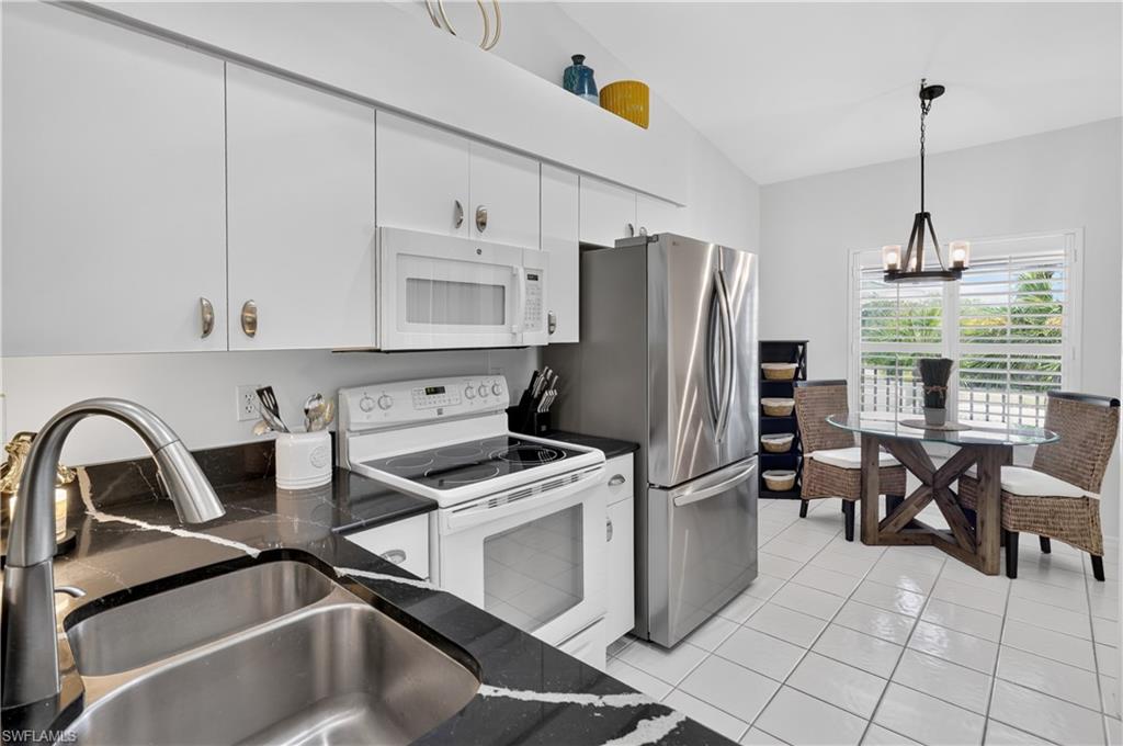 Kitchen featuring white cabinetry, stainless steel appliances, dark countertops with light veining, and tiled flooring