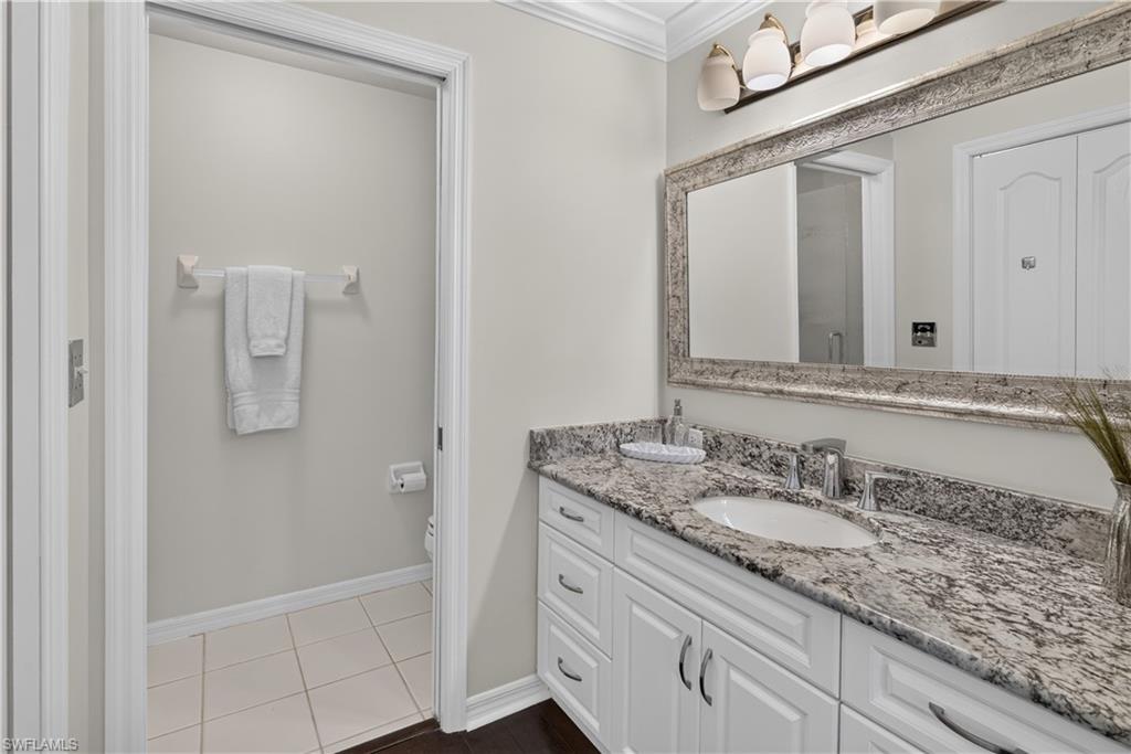 White vanity with shaker-style cabinetry, an integrated sink, and stone countertop