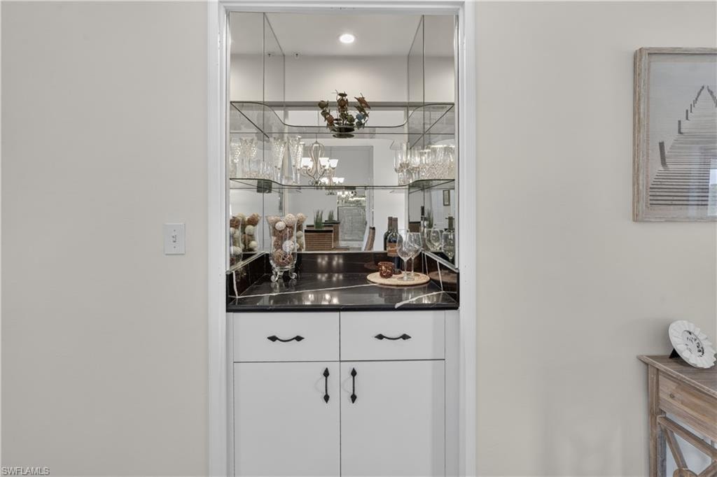 Built-in bar with white cabinetry, black countertop, mirrored back wall, and glass shelving