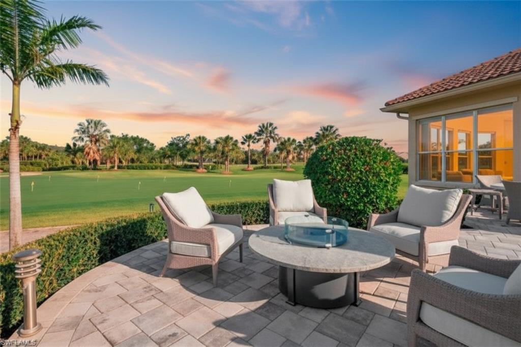 Paver patio with a fire pit table, surrounded by lush green landscaping and a golf course