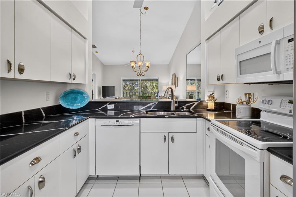 White cabinetry with brushed nickel hardware, black countertops with white veining, white tile flooring, and integrated white appliances