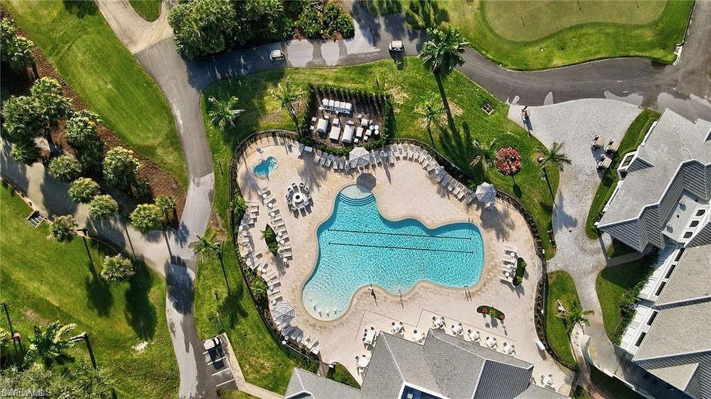 Large freeform swimming pool with integrated spa, expansive paver deck, surrounding green spaces, and adjacent multi-story residential structures