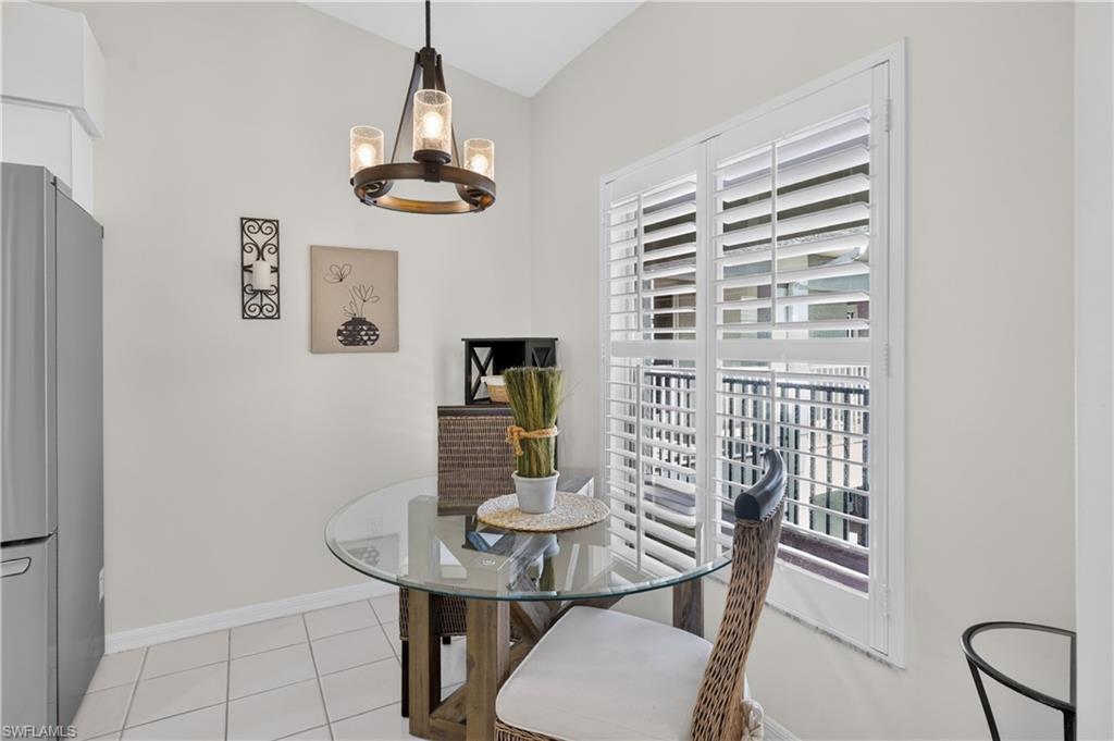 Vaulted ceiling with a contemporary chandelier, stainless steel refrigerator, plantation shutters, and tiled flooring