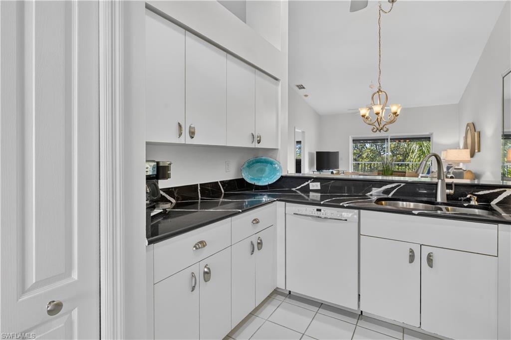 Kitchen featuring white cabinetry, dark countertops with light veining, stainless steel sink with gooseneck faucet, white built-in dishwasher, and white tile flooring