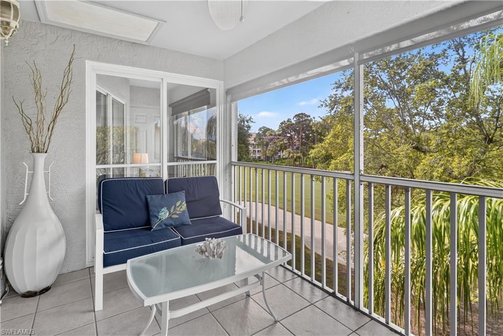 Screened balcony with tile flooring and a white railing overlooking trees and a paved path