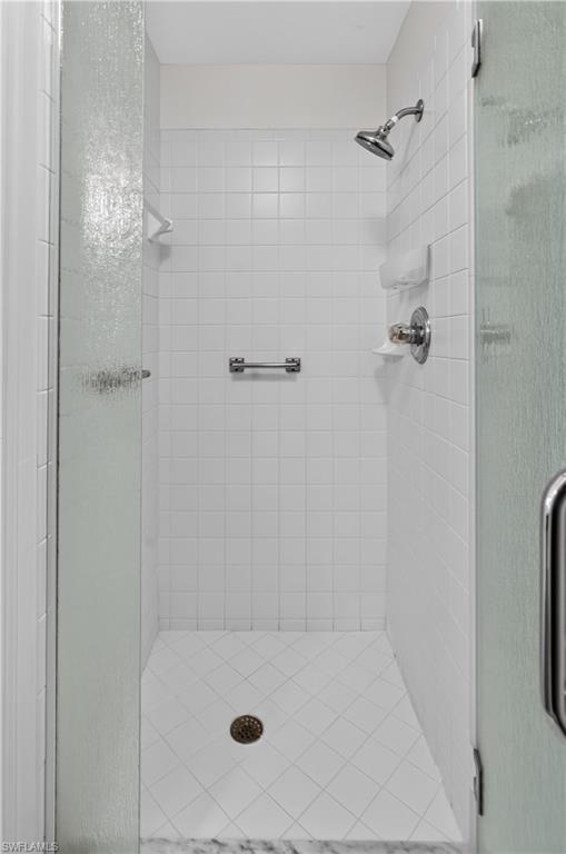 Modern walk-in shower featuring white subway tile walls, a rainfall showerhead with secondary wall-mounted fixture, chrome hardware, a linear drain system integrated into the white tile floor, and a frameless glass enclosure with brushed metal hardware