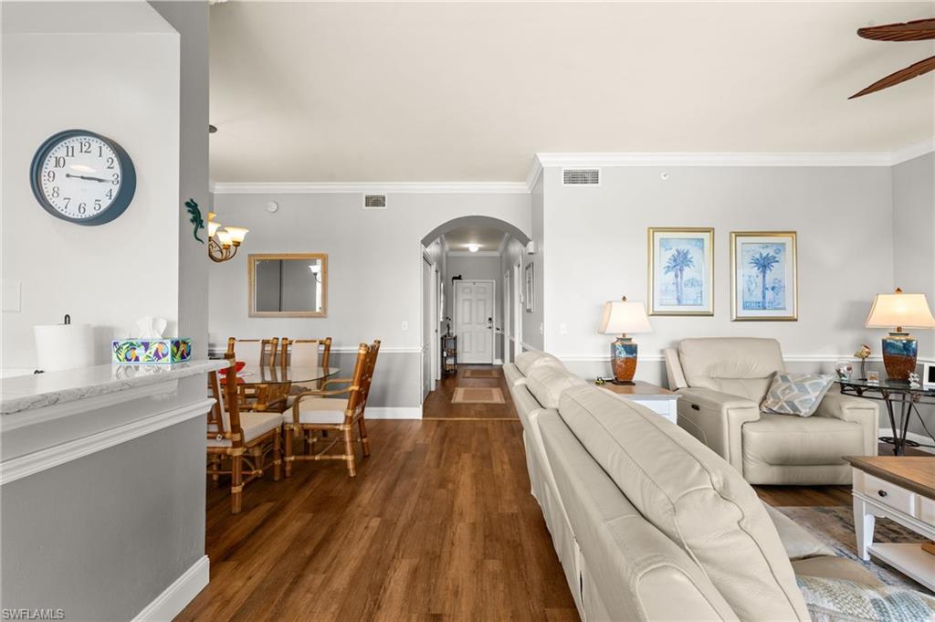 Open-concept living space with wood-finish flooring, crown molding, and a vaulted ceiling