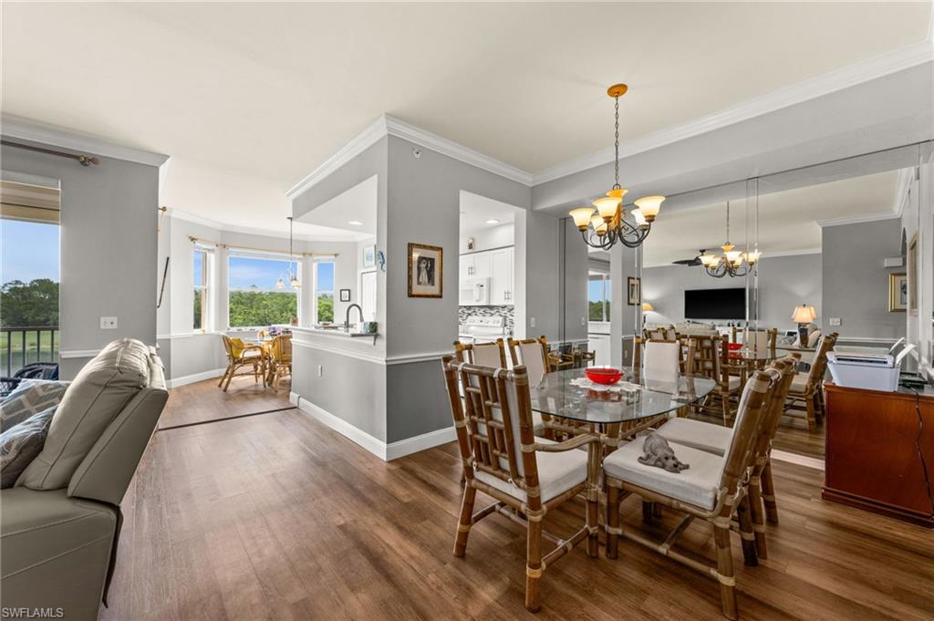 Open concept living space featuring wood-finish flooring, a contemporary chandelier, a mirrored wall, and crown molding