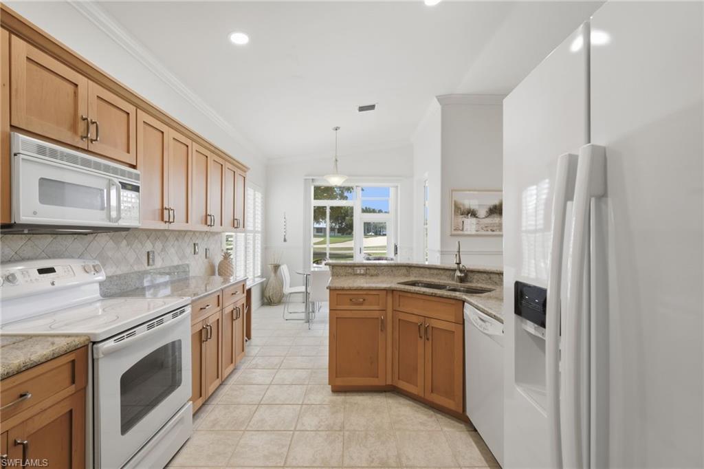 The beautifully appointed kitchen showcases warm honey-toned Shaker-style cabinetry accented with new hardware, crisp white appliances, elegant granite countertops, and a timeless tumbled marble backsplash, all complemented by serene golf course views that create an inviting backdrop for everyday living and entertaining.