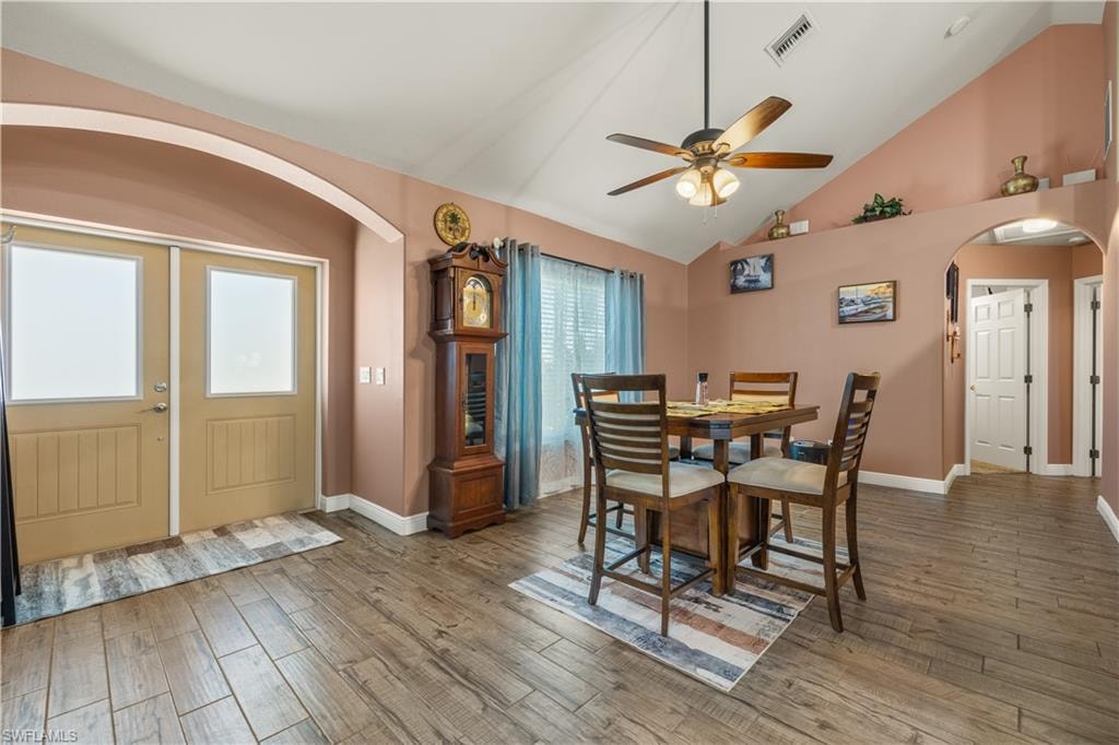 Entryway featuring double doors with frosted glass panels, wood-finish flooring, vaulted ceilings, and an arched doorway leading to an interior space