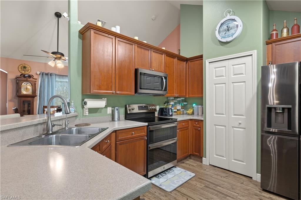Kitchen featuring wood-finish cabinetry, stainless steel appliances, a double basin sink, and wood-finish flooring