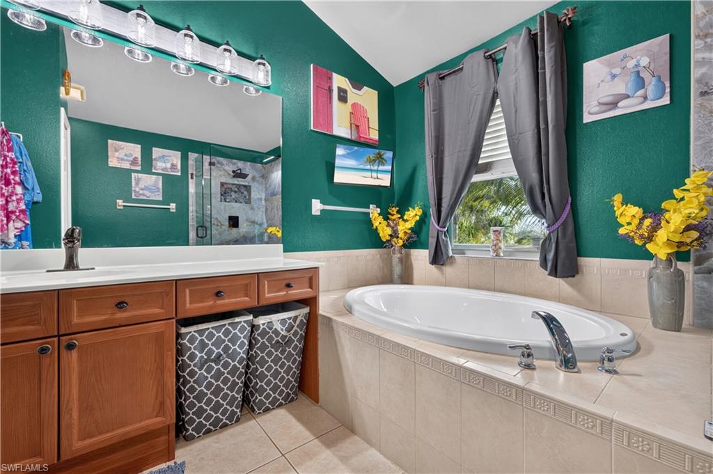 Bathroom featuring an integrated soaking tub with tile surround, a built-in wood-finish vanity with a single sink and white countertop, and a separate glass-enclosed shower with tile walls