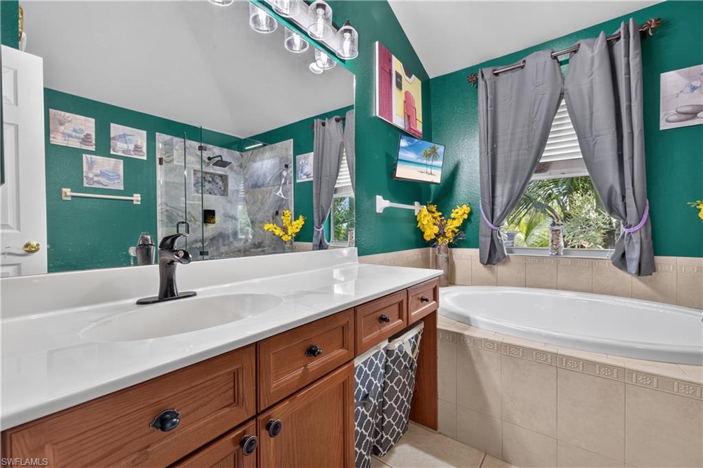 Bathroom featuring a built-in soaking tub, a stand-up shower with glass enclosure, a vanity with a white countertop and wood-finish cabinetry, and a window with natural light