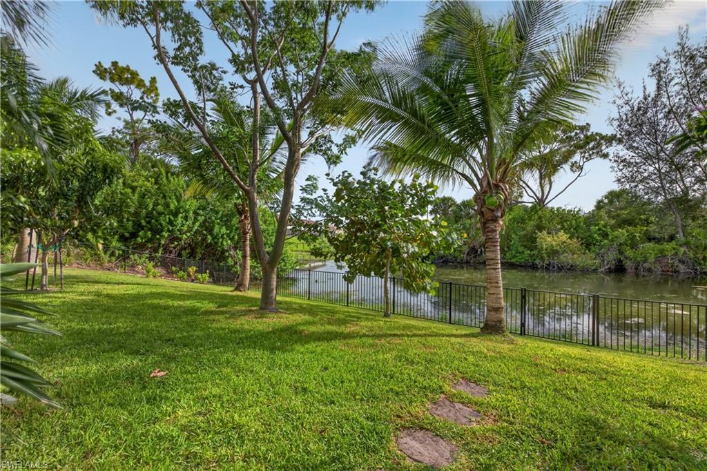 Lush green lawn with mature trees and stepping stones, featuring a black metal fence bordering a natural waterway