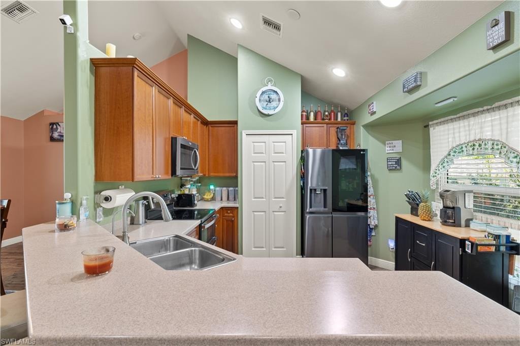 Kitchen featuring vaulted ceilings, wood-finish cabinetry, a double basin stainless steel sink, and a built-in microwave