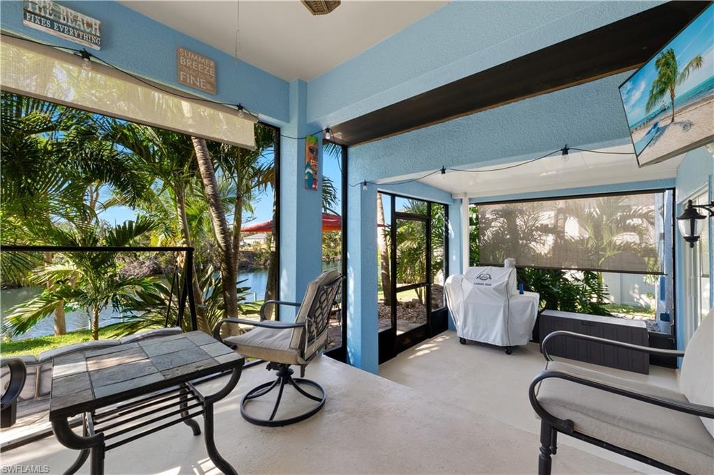 Screened lanai featuring a waterside setting, overhead string lighting, a wall-mounted flat-screen television, and roller shade privacy screens