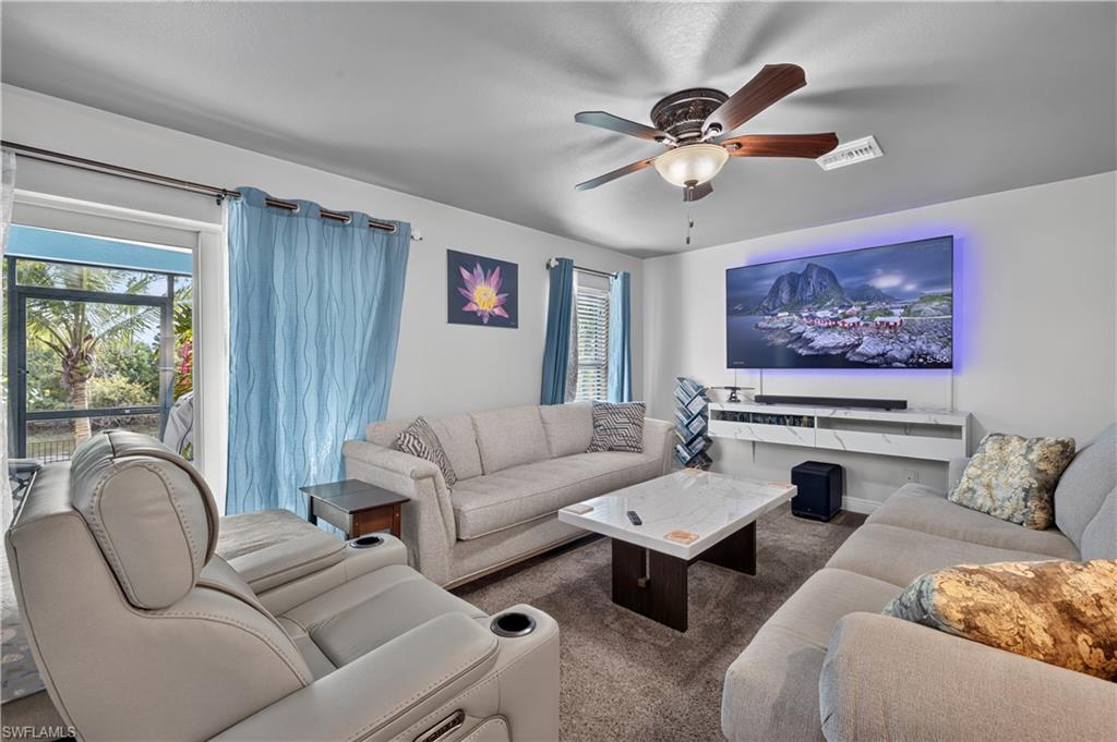 Spacious living area featuring neutral wall tones, carpeted flooring, and a large ceiling fan with integrated lighting