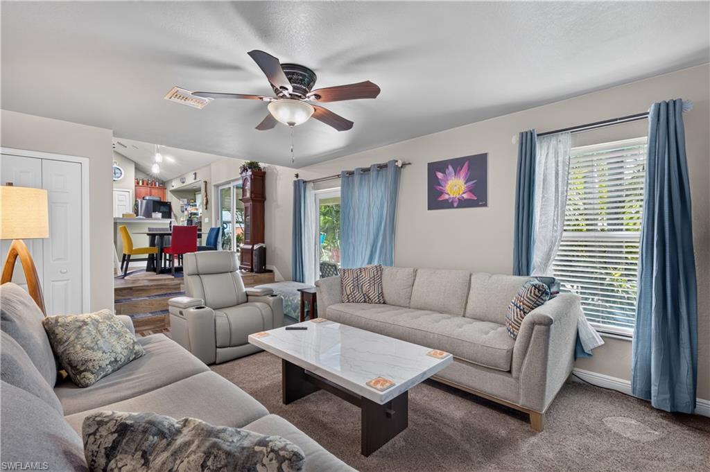 Carpeted living area featuring a ceiling fan, white paneled doors, and large windows with horizontal blinds