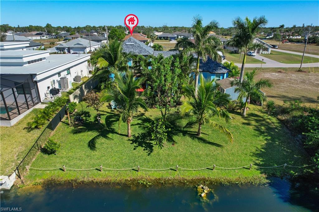 Expansive waterfront property featuring a lush green lawn, mature palm trees, a dedicated outdoor space, and a rope and post barrier along the water's edge